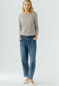 Gestreiftes Langarmhemd in Grau und Weiß; blaue Jeans mit großen Taschen und lockerer Passform; hellfarbene Schuhe.