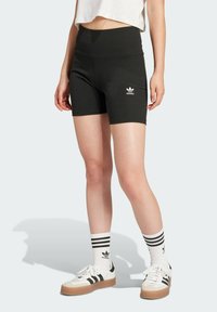 Black ribbed athletic shorts with high waistband, featuring a white Adidas logo on the left leg. Worn with white sneakers and striped socks.