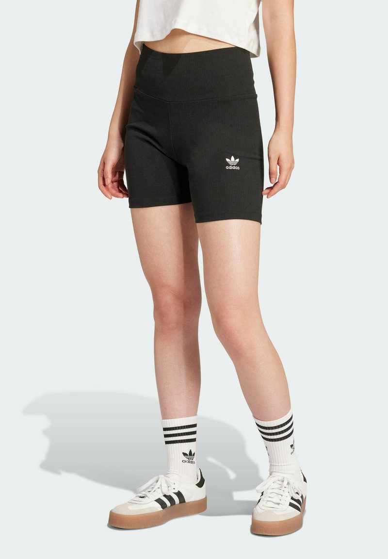 Black ribbed athletic shorts with high waistband, featuring a white Adidas logo on the left leg. Worn with white sneakers and striped socks.