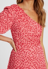 Červené šaty s květinovým vzorem a jedním ramínkem. Vyrobeno z lehkého materiálu, s nabíranými rukávy a přiléhavým pasem.