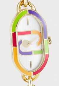 Montre dorée avec un cadran ovale ; décorée d'accents multicolores en vert, violet, rose et orange ; cadran blanc avec des index horaires métalliques.