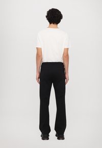 Black trousers with a relaxed fit and elastic waistband, paired with a plain white t-shirt, viewed from the back.