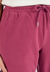 Fleece joggers in een rijke magentakleur met een elastische tailleband, verstelbaar trekkoord en zijzakken. Zacht, gestructureerd materiaal.