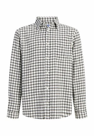 Teenagedreng stående iført en sort denimjakke, sort ternet skjorte over en rød top, sorte bukser og brune arbejdstøvler på en ensfarvet baggrund.