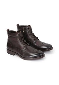 Botas de tobillo de cuero marrón oscuro con cordones en la parte frontal, cremallera lateral, detalles de brogue en la puntera, tacón plano y textura suave.
