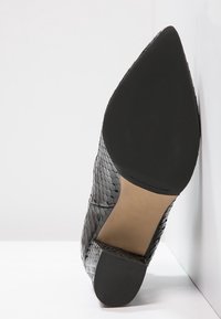 Zapato de cuero trenzado negro con punta afilada y parte superior texturizada. La suela es de goma negra con un borde ligeramente elevado.