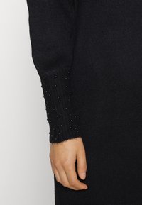 Svart stickad tröja med ribbad mudd prydd med svarta pärlansatser. Tyget har en mjuk struktur och en figurnära silhuett.