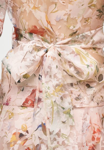 Robe fleurie transparente avec une teinte rose douce, dotée d'un lien à l'arrière, de motifs floraux délicats et d'un tissu léger et texturé.