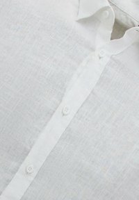 Witte linnen blouse met een gestructureerde afwerking, voorzien van een klassieke kraag en een vijfknopssluiting aan de voorkant. Eenvoudig en strak ontwerp.