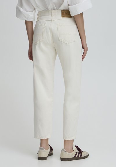 Pantalons blancs taille haute à coupe droite, avec poches arrière et étiquette en cuir beige. Associés à des baskets claires.