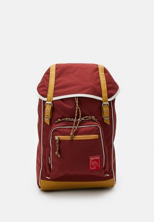 Roter Canvas-Rucksack mit kontrastierenden gelben Trägern und Akzenten, einer Fronttasche, verstellbarem Kordelzug und weißen Paspelierungen.