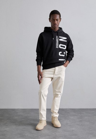 Schwarzer Hoodie mit weißem "ICON"-Grafik, cremefarbene Jeans und hellbeige Sneaker. Lässig, entspannte Passform mit Kapuze und Kordelzug.