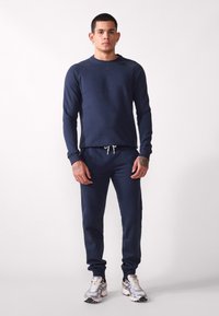 Navy blue sweatshirt with long sleeves, crew neck, and ribbed cuffs, paired with matching joggers featuring an elastic waistband and drawstring.