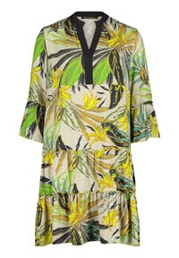 Robe florale avec un col noir, des manches courtes en forme de cloche et un ourlet à volants superposés. Présente un motif de feuilles tropicales jaunes et vertes sur un fond crème.