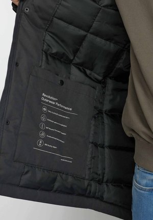Zwarte pufferjas binnenkant met doorgestikte textuur. Bevat een label met gedetailleerde materiaalspecificaties; inclusief waterdicht weefsel en SBS-rits.