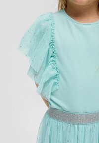 Een lichtgroene top met gerimpelde tule mouwen met zilveren stippen en een bijpassende rok met een glinsterende tailleband.