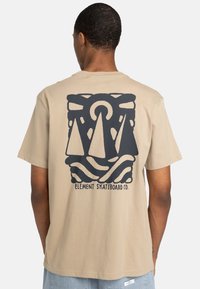 Beige Baumwoll-T-Shirt mit einem großen schwarzen Grafikdesign von zwei dreieckigen Formen und wellenförmigen Linien, mit dem Text "Element Skateboard Co." darunter.
