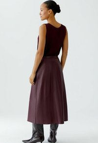 Bordeaux mouwloos topje gecombineerd met een lange bordeaux leren rok; gedetailleerd stikwerk en een gematteerde afwerking; gedragen met glanzende zwarte laarzen.