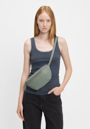 Jasnozielona skórzana nerka o gładkiej fakturze i zamknięciu na zamek, noszona na ciele. Casualowy strój składający się z ciemnego topu na ramiączkach i dżinsów.