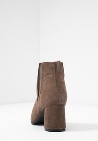 Bottine en suede marron avec un talon carré et des panneaux latéraux élastiques. Elle possède un bout arrondi et une semelle lisse noire.