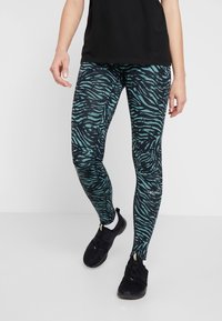 Stretchleggings i teal och svart zebramönster, med en slät yta och en tight design. Bärs med svarta träningsskor.