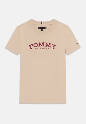 Bēša kokvilnas T-krekliņš ar sarkano "TOMMY HILFIGER" logo, apaļu kakla izgriezumu, īsām piedurknēm un mazu logo akcentu uz piedurknes.
