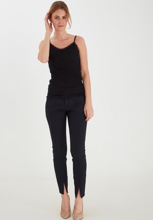Black camisole with lace trim, paired with fitted black pants featuring slit hems, complemented by nude high heels.