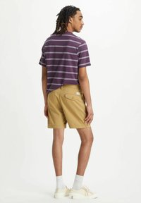 Lyhythihainen purppuraruudullinen paita rentoa mallia, yhdistettyinä khaki-shortsien kanssa. Shortseissa on takatasku ja hienovaraiset ompeluyksityiskohdat.
