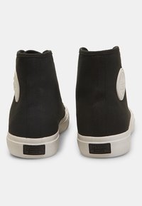 Crne platnene čizme do gležnja s elastičnim bočnim panelima, bijelim gumenim potplatima i okruglim logotipom na peti. Jednostavan i funkcionalan dizajn.