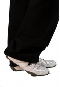 White athletic shoes with silver accents, featuring a textured sole, worn with black pants, which have a gathered cuff at the ankle.