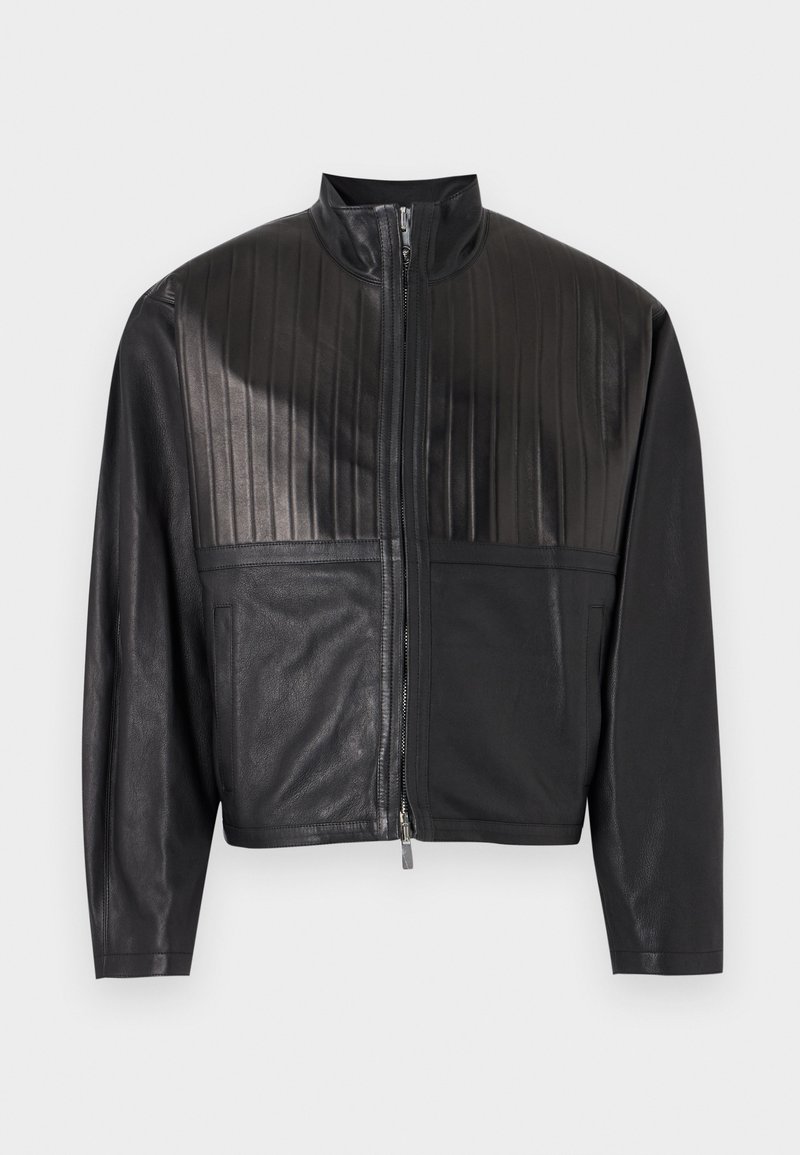 Schwarze Kunstlederjacke mit vertikal gesteppten Paneelen auf der Brust, Frontreißverschluss und zwei Seitentaschen, vor neutralem Hintergrund.