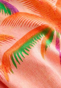 Zachte stof met een patroon van oranje, groene en paarse palmbladeren op een roze achtergrond, met textuur en zachte plooien zichtbaar.