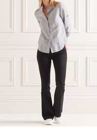 Camicia a righe blu chiaro e bianca con maniche arrotolate, abbinata a pantaloni neri svasati e sneaker bianche. Design minimalista.