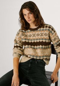 Gebreide trui met een beige, bruine en blauwe geometrische patroon, voorzien van een ronde halslijn en geribbelde manchetten. Draagt het met donkere jeans.