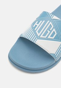 Sandal in gomma leggera blu chiaro con una larga fascia decorata con il logo "HUGO" in rilievo e accenti geometrici bianchi. Suola testurizzata per una migliore aderenza.