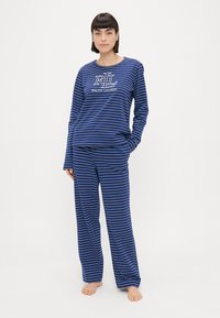 Námornícke modré pruhované pyžamo vyrobené z mäkkej tkaniny. Top s dlhými rukávmi obsahuje logo "RL" a text "Ralph Lauren"; voľné nohavice s elastickým pásom.