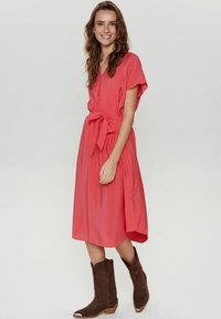 Rochie midi corai cu mâneci scurte, talie marcată și o siluetă fluidă. Purtați cu cizme cowboy maro, având un design cu vârf ascuțit.