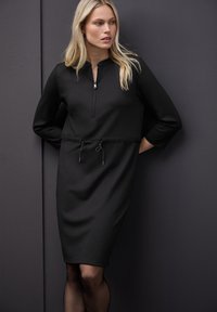 Schwarzes Kleid mit Halbreißverschluss-Kragen, Dreiviertelärmeln und gerafftem Taillendetail, aus einem glatten, strukturierten Stoff gefertigt. Schlichtes Design.