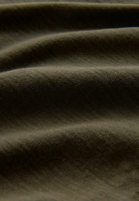 Strukturierter, olivgrüner Stoff mit sanften, wellenförmigen Mustern. Das Material wirkt robust mit matter Oberfläche und feinem Einschnittmuster.