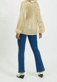 Blusa di crema con pieghe e motivo a pois multicolori, abbinata a jeans a campana blu e stivali bianchi con tacco a blocco.
