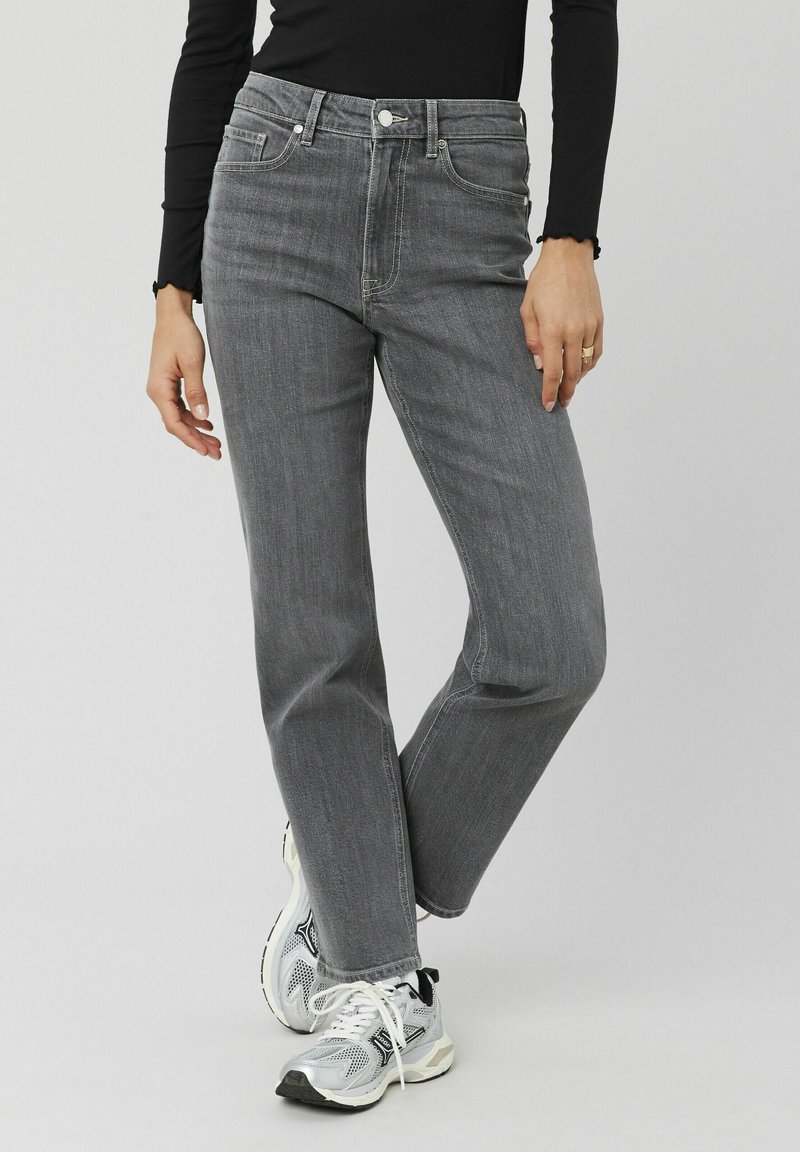 Jean en denim gris avec une coupe droite, cinq poches et une fermeture à bouton. Associé à des chaussures de sport grises et argentées.