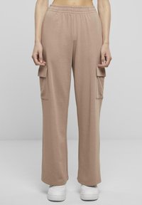 Beige cargobyxor med elastisk midja, vida ben och två sidofickor. Tillverkade av mjukt, töjbart tyg, tillsammans med vita sneakers.