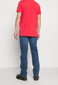 Rode T-shirt met korte mouwen, van katoen, casual pasvorm. Gemaakt met blauwe rechte jeans en zwarte schoenen. Eenvoudig ontwerp; geen zichtbare patronen.