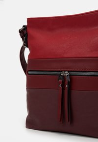 Rød læder crossover taske med struktureret overflade, kontrasterende mørkerød nederste sektion, lynlås lomme og justerbar rem.