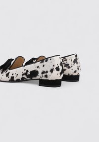 Zapatos planos con un patrón de piel de vaca en blanco y negro, con un lazo negro como acento y un tacón bajo y resistente para mayor comodidad.