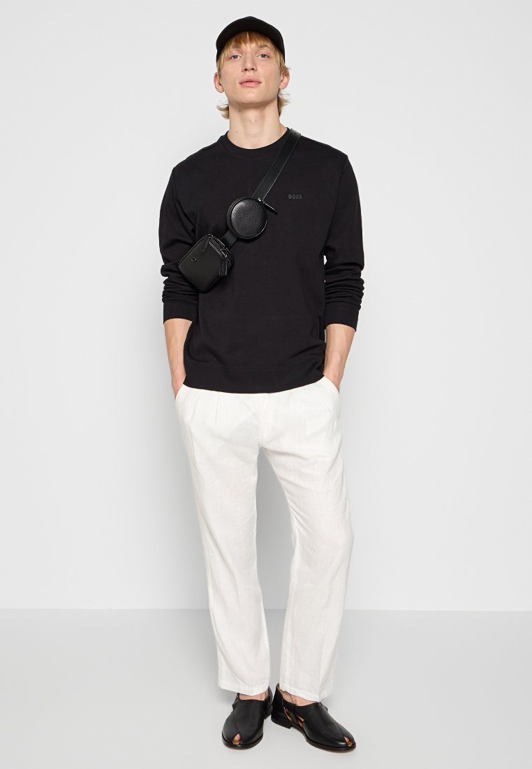 Zwart langemouwen shirt, witte linnen broek, zwarte sandalen en zwarte schoudertas. Eenvoudig ontwerp, relaxte pasvorm, met soepele texturen.