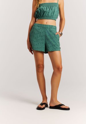 Groen katoenen tweedelig outfit met een gesmokte cropped top en bijpassende korte broek met bloemrijke oogletdetails, gecombineerd met zwarte slippers.