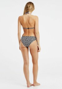 Sort bikini med hvidt blomsterprint, halterneck-top og matchende højtaljede bund. Glat tekstur, minimalistisk dækning.