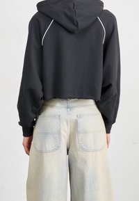 Przycięta czarna bluza z kapturem o teksturowanym wykończeniu i białym akcentem szycia, w połączeniu z jasnoniebieskimi, wyblakłymi, szerokimi dżinsami z dwoma tylnymi kieszeniami.