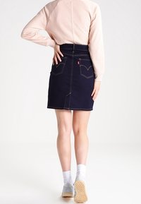 Mörkblå denimkjol med bakfickor, synlig sömnad och hög midja. Kombinerad med en ljusrosa sweatshirts och vita strumpor.